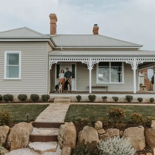 a couple and a dog standing in front of a house